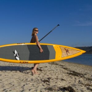 Woman standing on the shore holding ayellow Hobie Elite touring paddleboard.