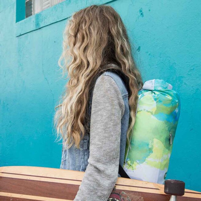 A girl holding a skateboard with the devoe IceMule 9L cooler on her back.