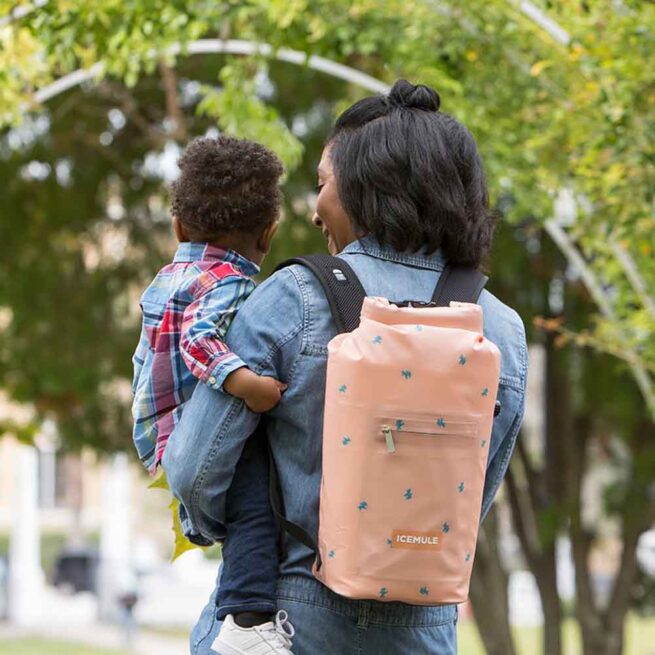 A lady wih a child in her arms and the IceMule Jaunt sunset mule cooler on her back.