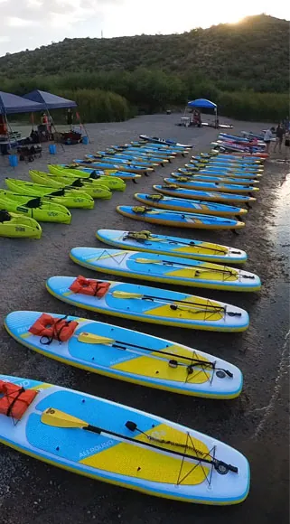 Colorful kayaks and paddleboards lined up lakeside.
