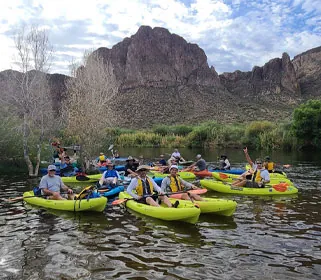 Group kayaking on scenic waters with a mountain background. Riverbound Paddle Company Group Event