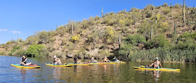 People kayaking on river with desert landscape.