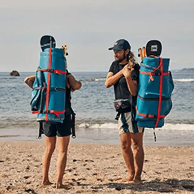 Two backpackers with gear on a beach preparing for hike.