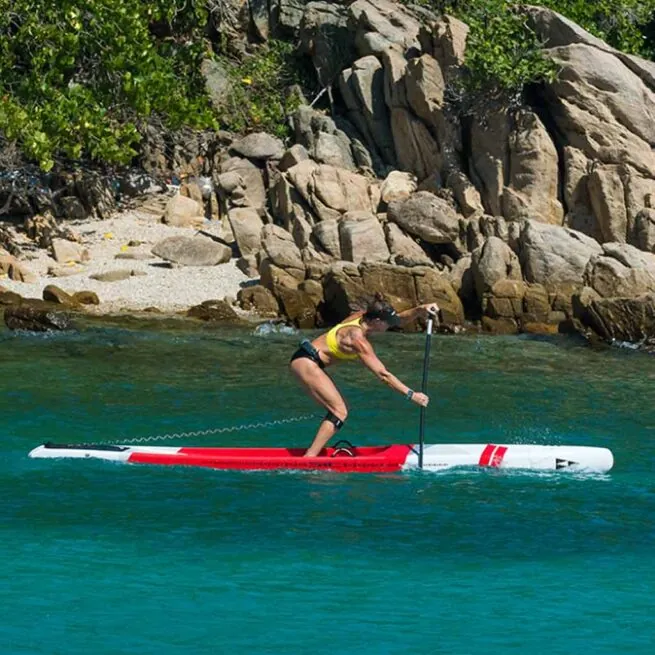 Woman paddleboarding near rocky shore in clear blue water.