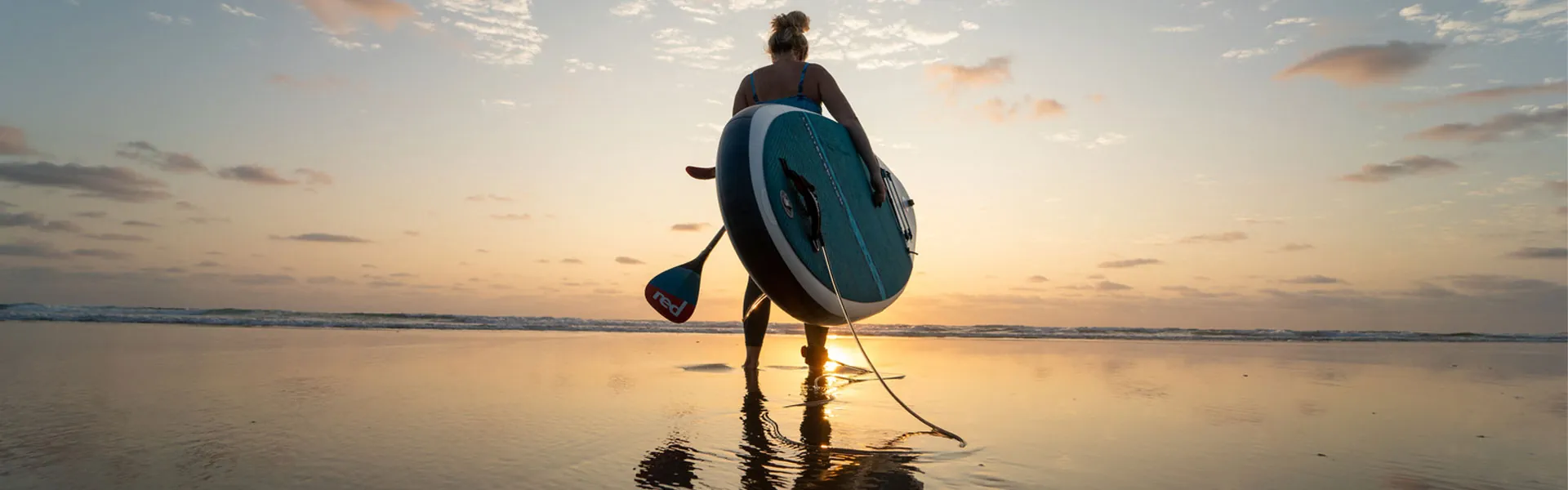 Red Paddle Co Inflatable SUP with a girl on the beach at sunset. Riverbound SPorts Red Paddle Co dealer in Tempe, Arizona.