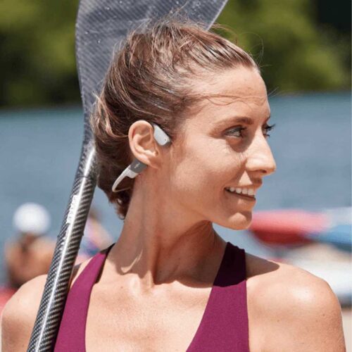 Woman with earbuds playing tennis in sunny weather