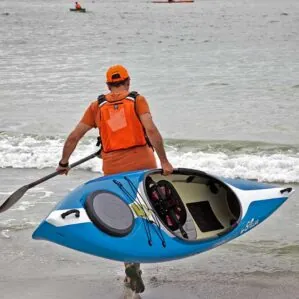 Man carrying blue kayak into the ocean