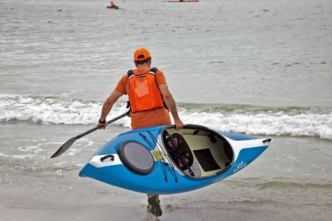 Man carrying blue kayak into the ocean