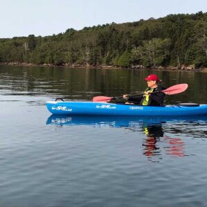 Person kayaking on calm lake with forest backdrop