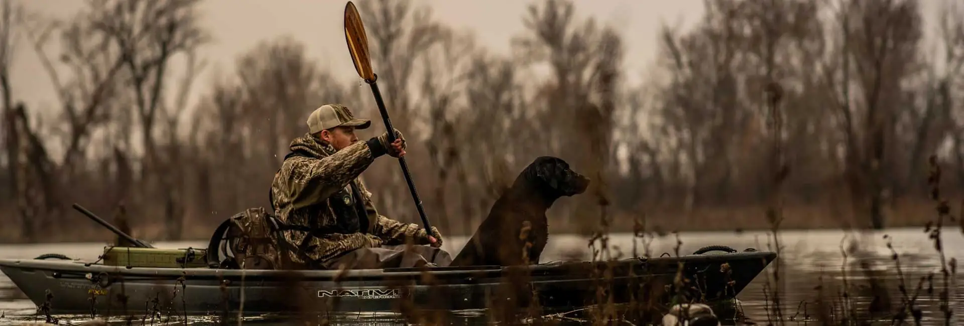 Man and dog kayaking in the Native FX 12 in serene, tree-lined waters. Riverbound Sports