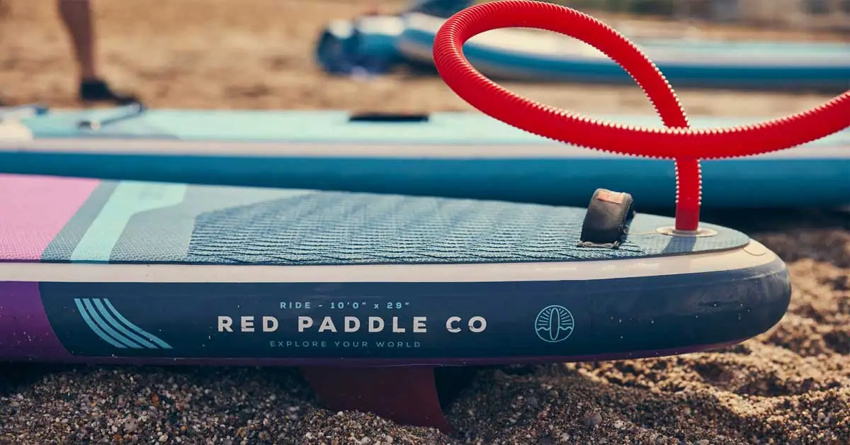 Inflatable paddle board with foot pump on beach.