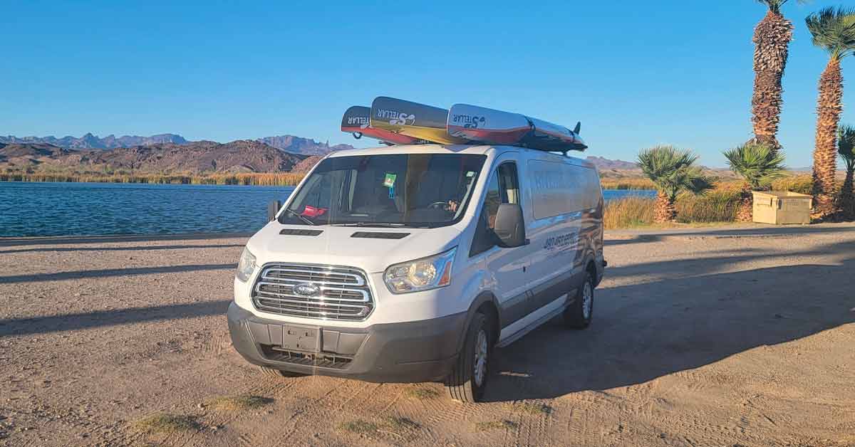 Van with kayaks parked by a lake at sunset