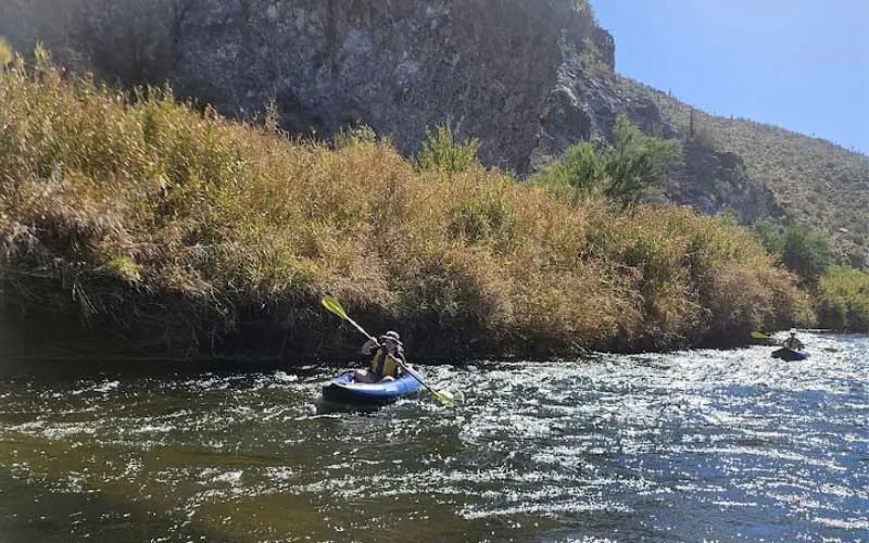 Person kayaking on river with lush riverbanks