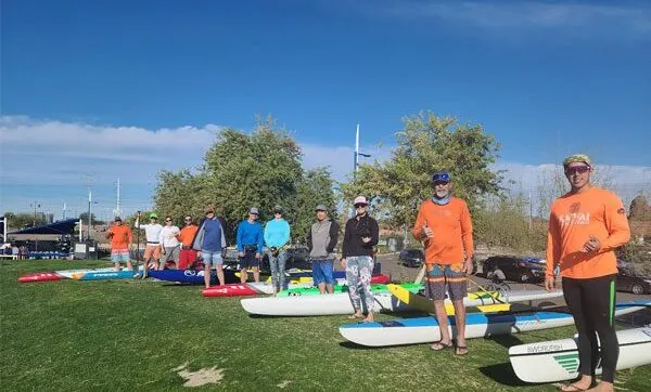 Group of people with paddleboards on grassy field. Tempe Town Lake Fitness Paddle.