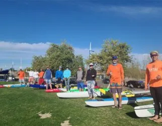 Group of people with paddleboards on grassy field. Tempe Town Lake Fitness Paddle.